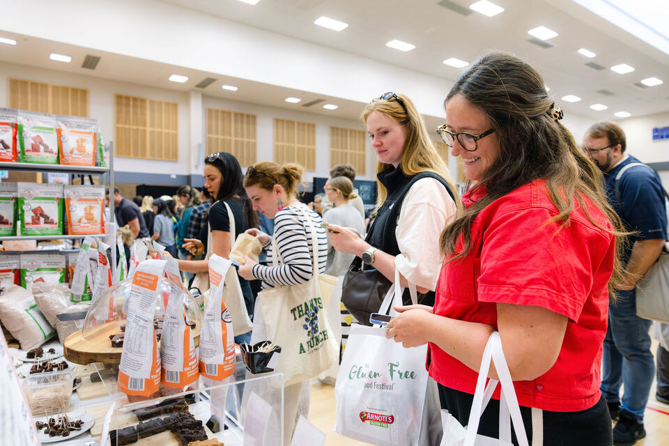 Visitors browsing a stall at the Gluten Free Food Festival, carrying festival tote bags